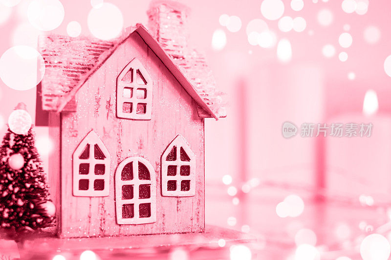 A toy house on the background of burning candles. Accessories on Christmas Day and New Year's Day. Christmas background. Ð¡olor Viva Magenta. Demonstrating the colors of 2023.